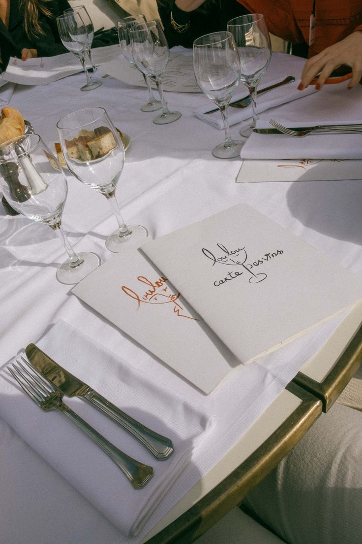 a table with wine glasses, silverware and menus on it at an outdoor restaurant