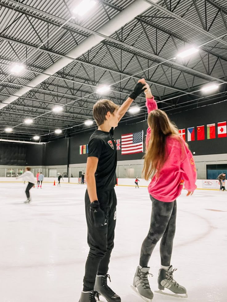 two people standing on an ice rink holding their hands up in the air as they skate