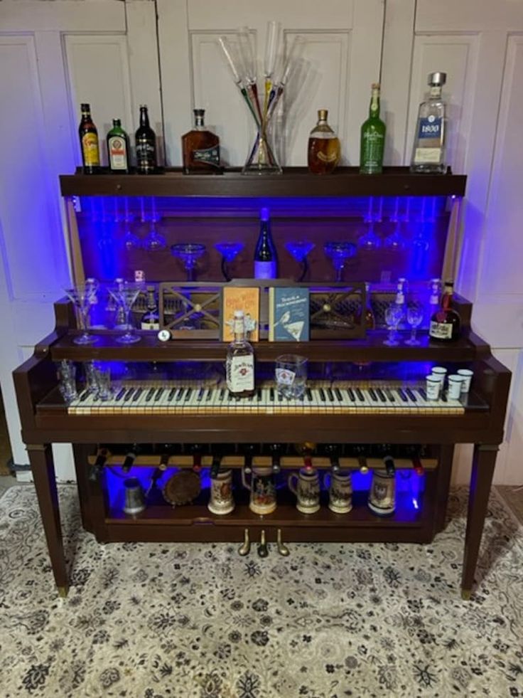 an upright piano is illuminated with blue lights and liquor bottles on the shelf above it