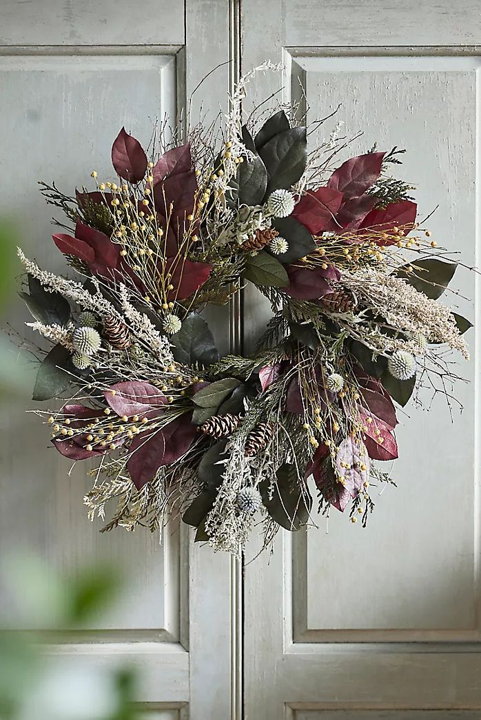 a wreath is hanging on the front door with flowers and greenery in fall colors