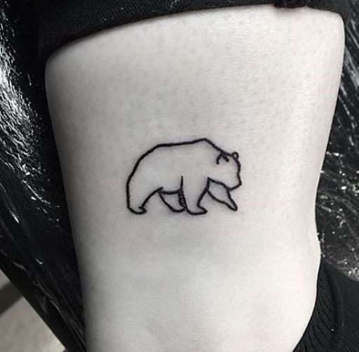 a small bear tattoo on the side of a woman's leg, with black ink