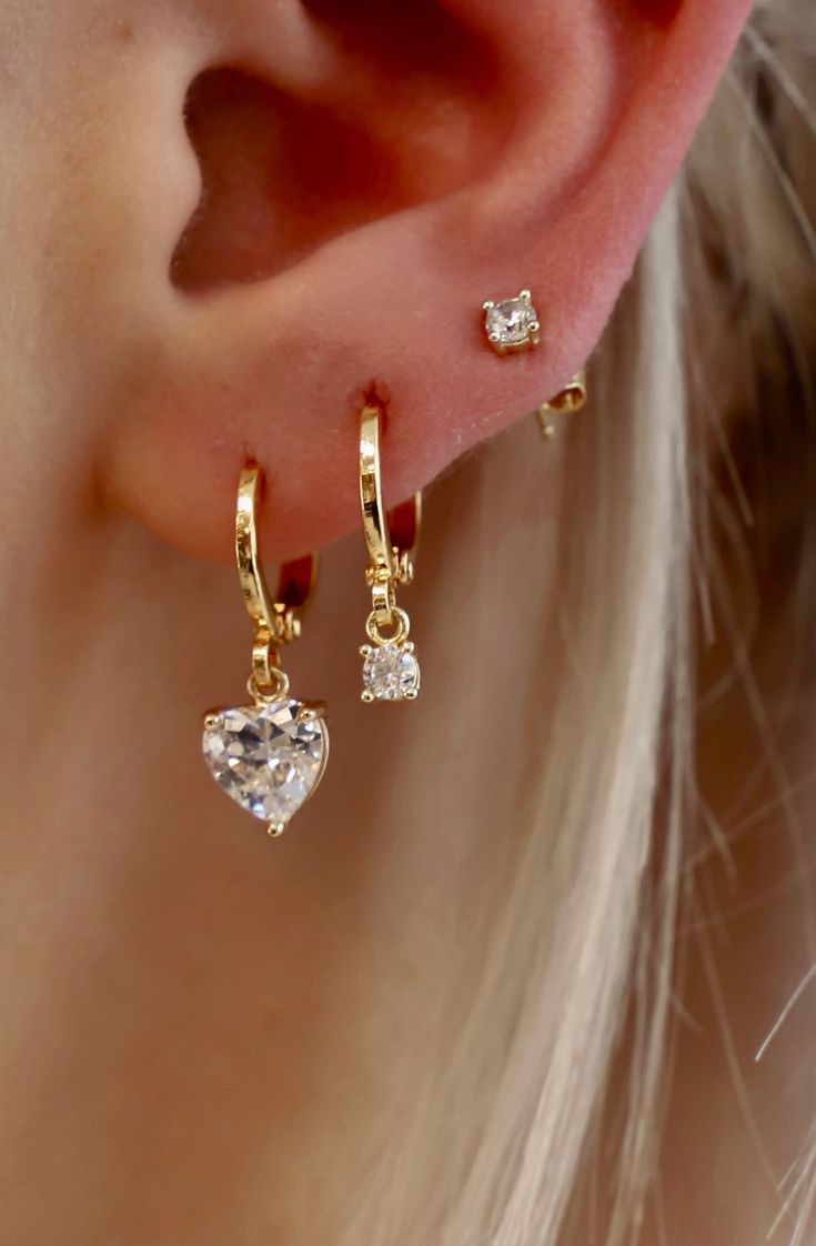 This CZ Heart Huggie ﻿is a fun yet sophisticated earring. These would look darling alone or stack with some of our studs to create a shiny layered look. Materials: Cz heart charm, gold plate brass huggies SKU: E1545G Three Hoop Ear Piercings, Stacked Earrings Gold, Heart Earrings Gold, Dainty Huggie Earrings With Heart Charm, Gold Dainty Heart Earrings With Cubic Zirconia, Gold Cubic Zirconia Heart Earrings In Dainty Style, Dainty Gold Heart Earrings With Cubic Zirconia, Gold Heart Cartilage Earrings For Everyday, Everyday Gold Heart Cartilage Earrings