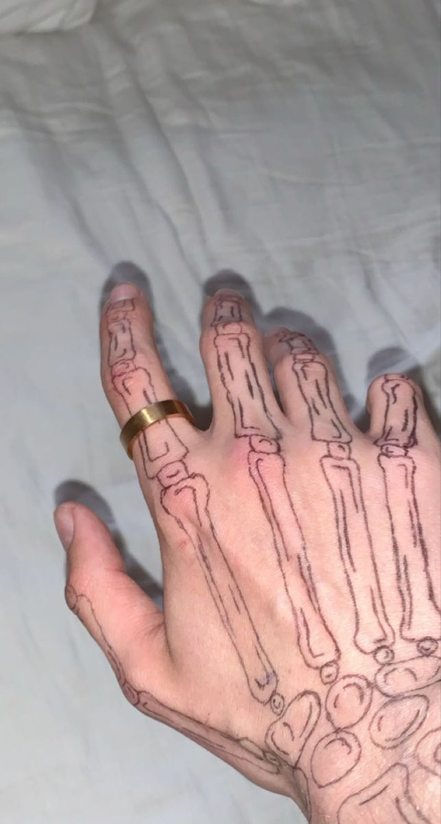 a person's hand with tattoos on it, holding something in one hand and wearing a gold ring