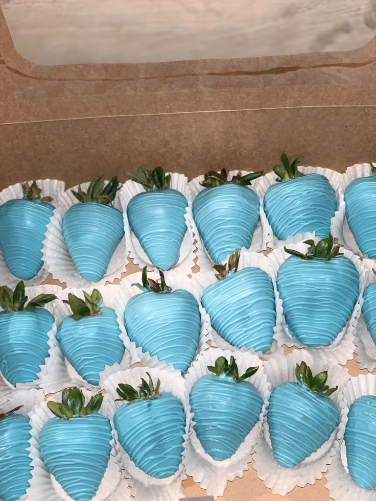 a box full of blue chocolate covered strawberries with green leaves on the top and bottom