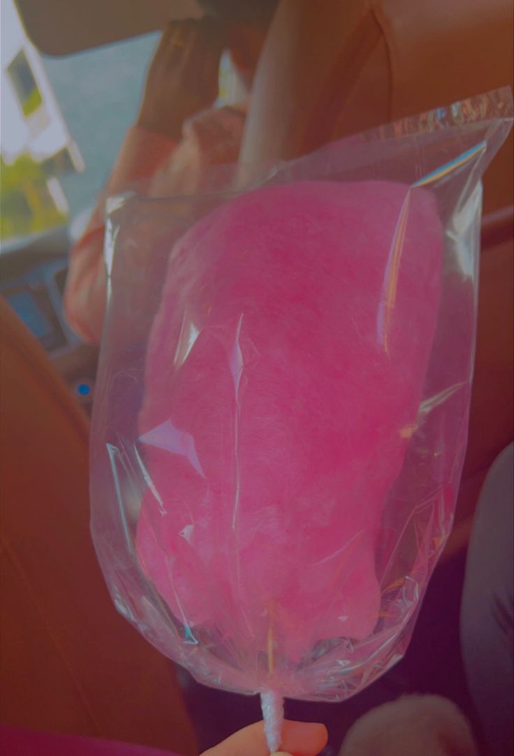 a person holding up a pink lollipop in a plastic bag on the back seat of a car