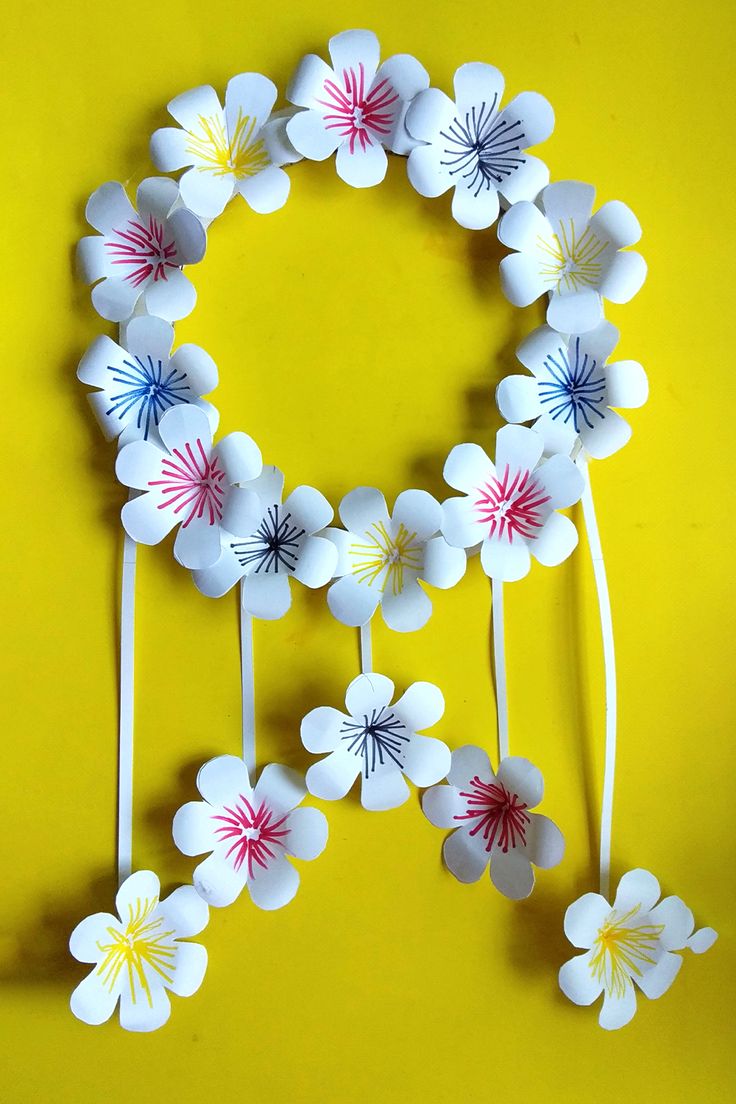 paper flowers are arranged in the shape of a circle on a yellow background with white sticks