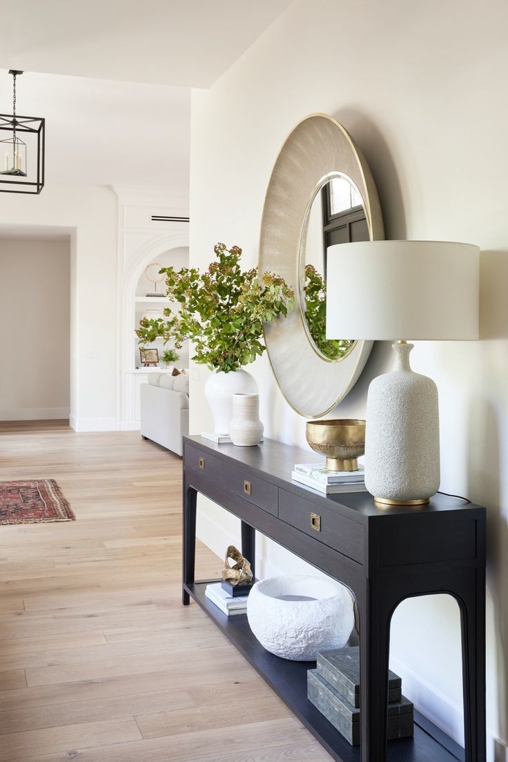 a table with a mirror, lamp and vase on it in a room that has hardwood floors