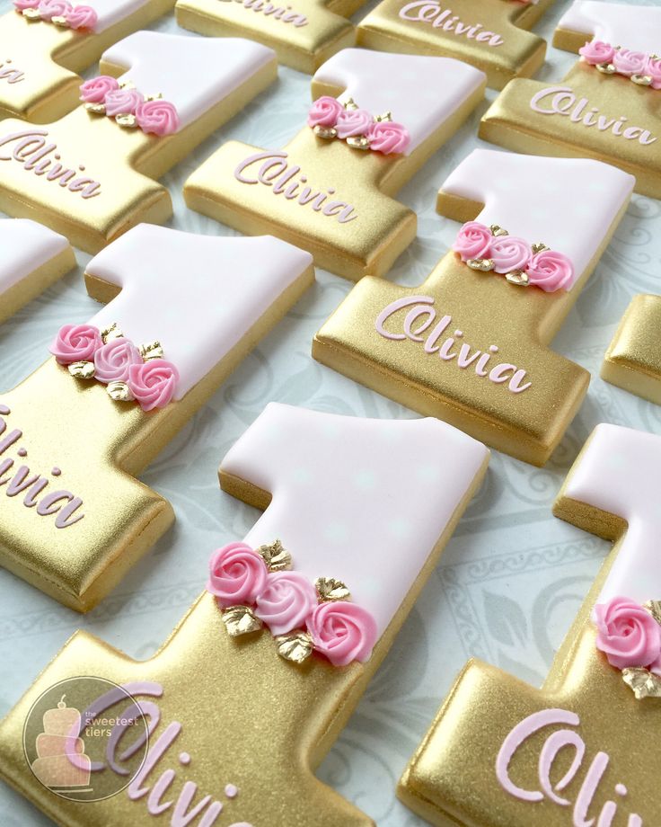 pink and gold decorated cookies are arranged on a white tablecloth with name tags in the shape of letters