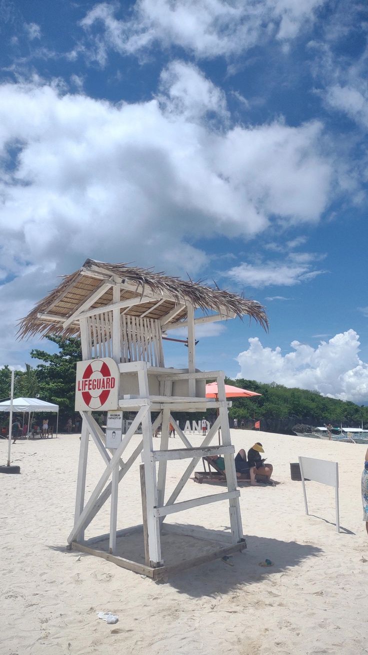 a lifeguard tower on the beach with people sitting under it