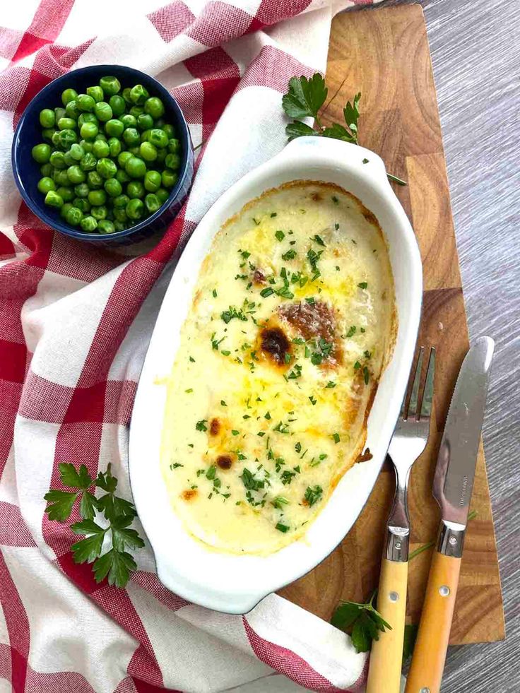 a casserole dish with peas and meat in it on a red and white checkered table cloth