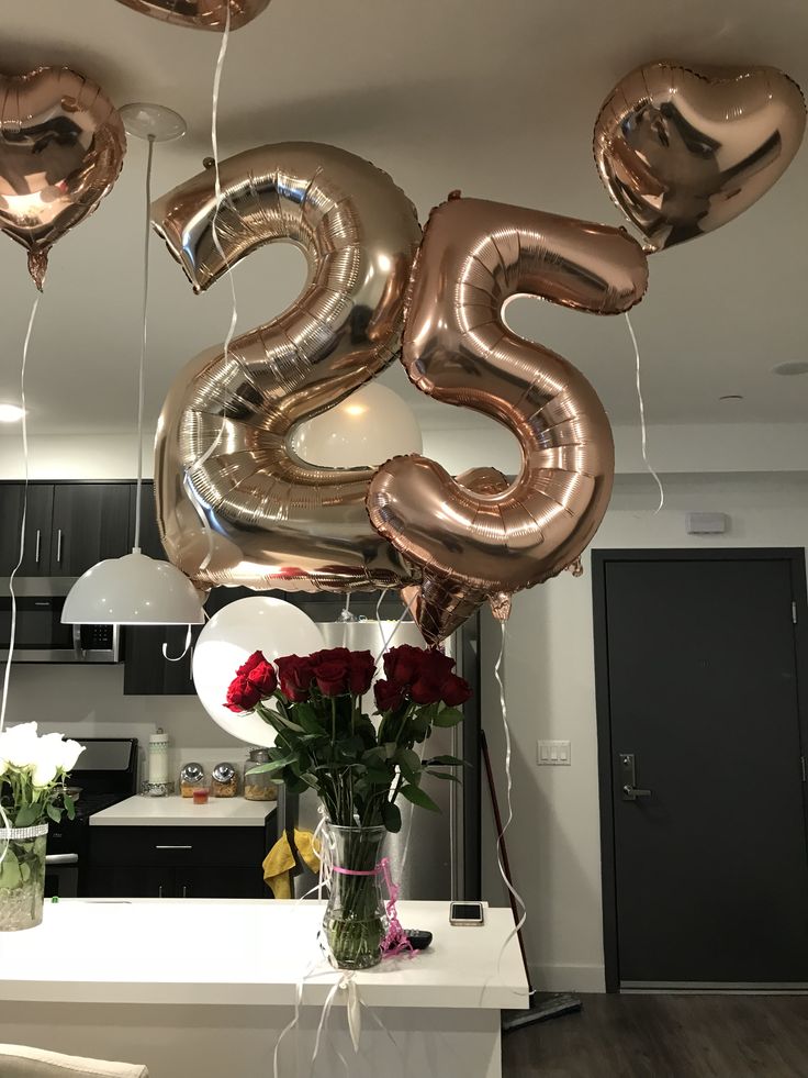 some balloons that are shaped like the numbers twenty five and two roses in vases