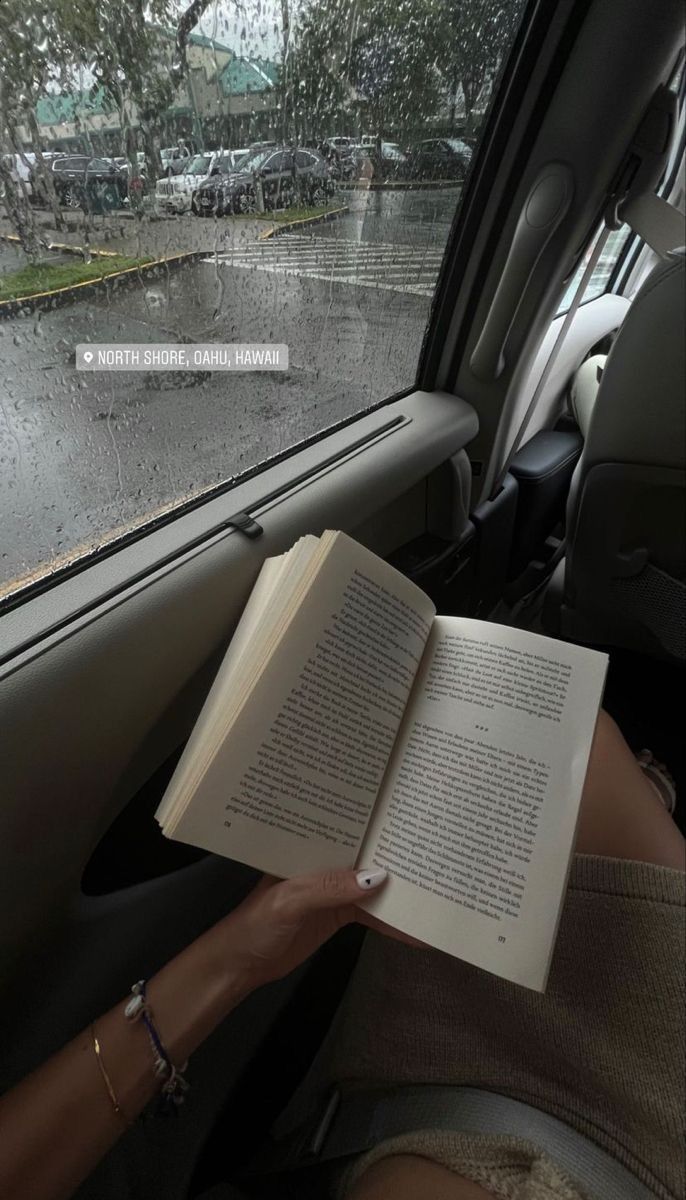 a woman reading a book in the back seat of a car on a rainy day