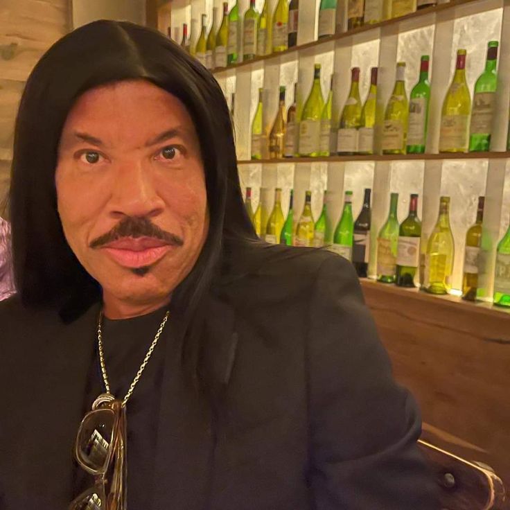 a man with a moustache on his face sitting in front of wine bottles