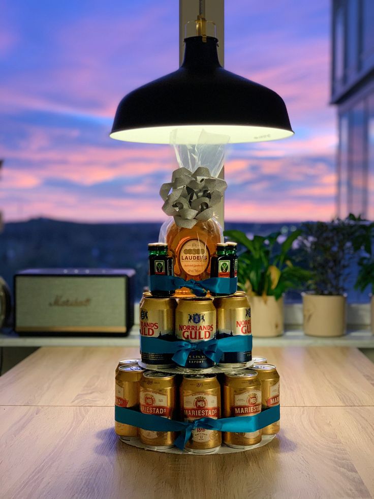 a stack of beer cans sitting on top of a wooden table next to a lamp