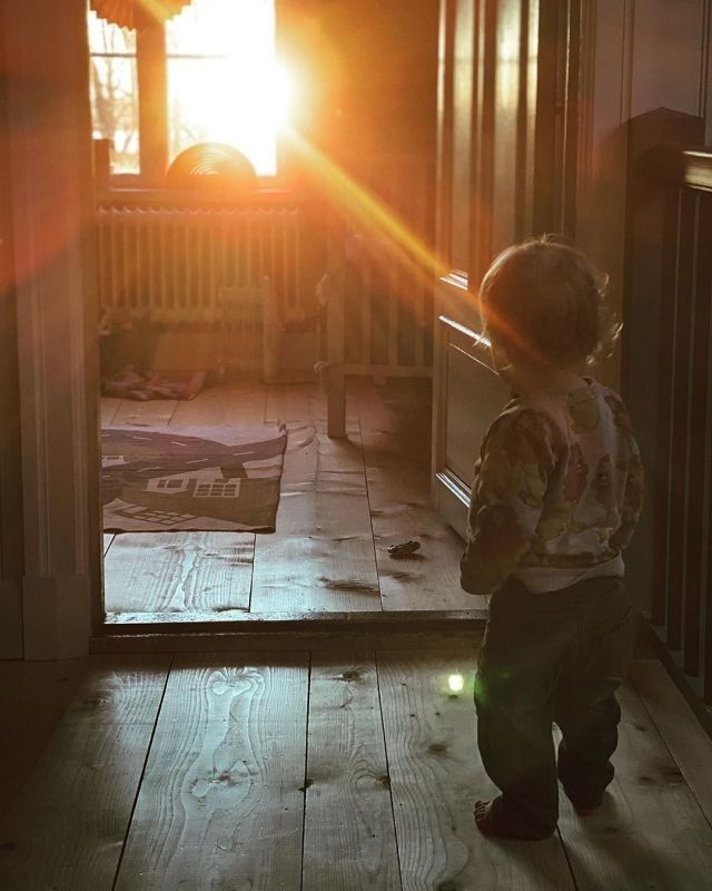 a little boy standing in front of a door with the sun shining through it's window