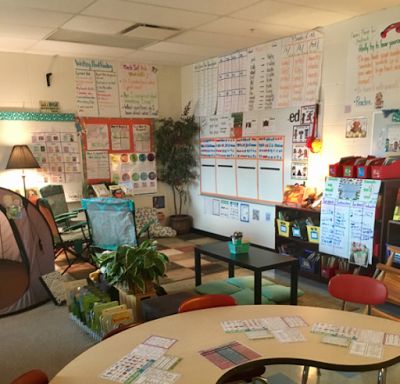 a classroom with desks, chairs and a tent in the back ground is full of books