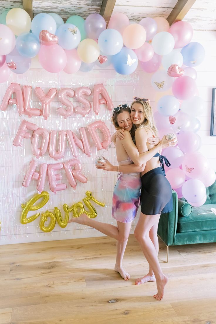 two women hugging each other in front of balloons