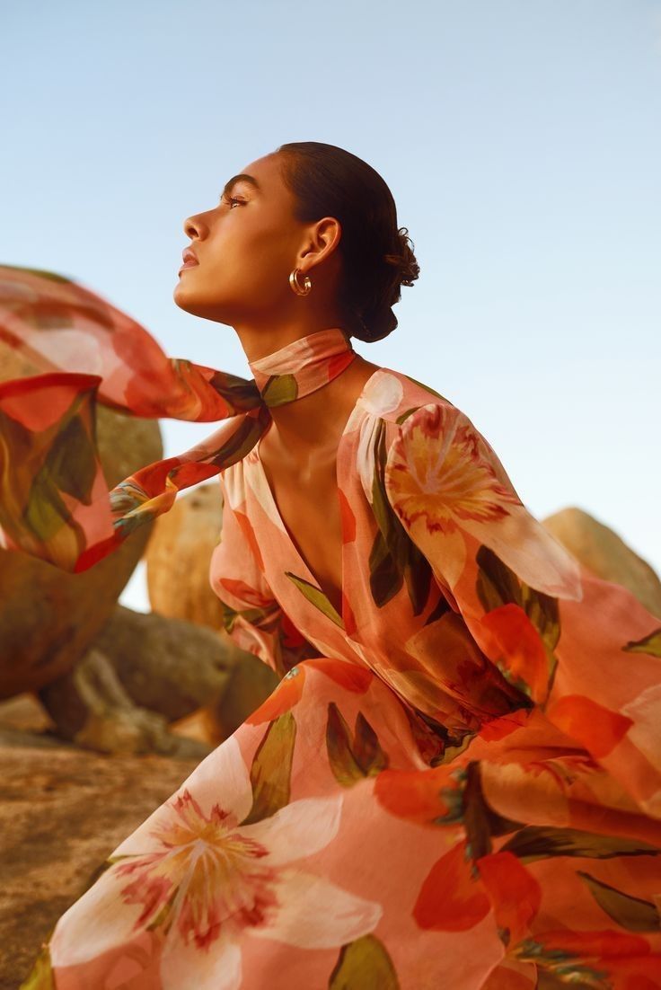 a woman sitting on top of a rock next to a desert area wearing a pink dress