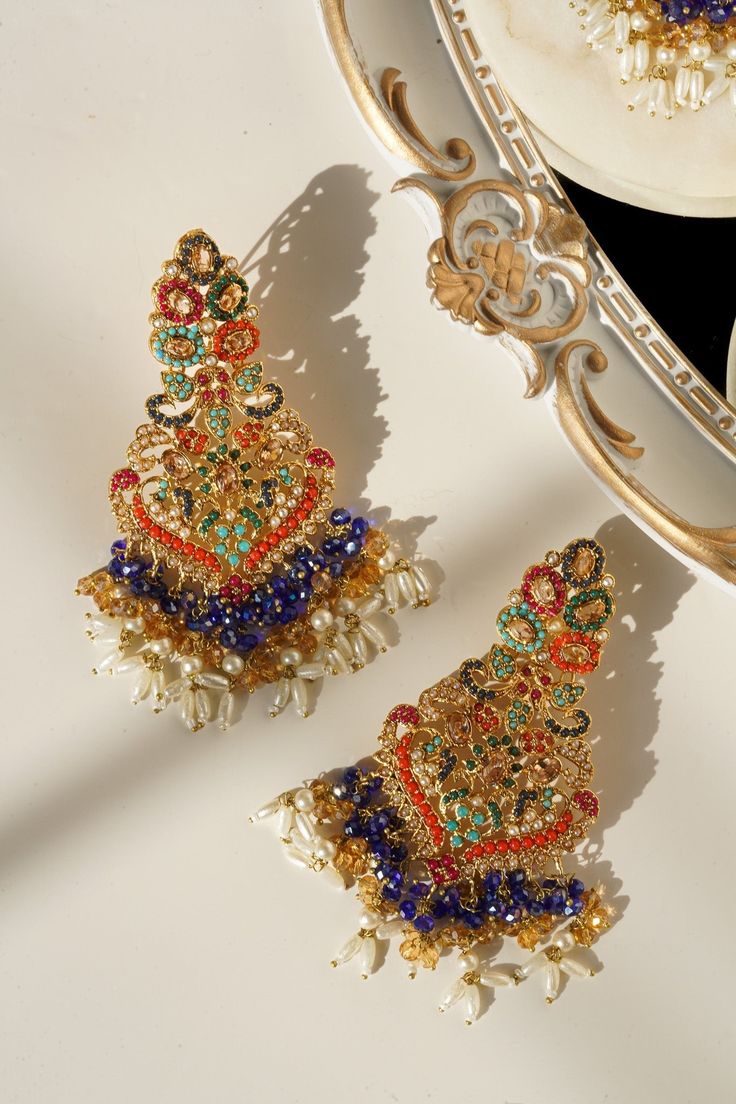 Elevate your festive attire to dreamy perfection with the Sarah - Chandelier Earrings & Maang Tikka Set, an embodiment of grandeur and allure. This exquisite earrings & maang tikka set is meticulously embellished with the splendor of multi-color stones and embellishments, adding a touch of magic to your look. The set includes a pair of stunning chandelier earrings and a maang tikka, each designed to captivate. With an approximate earring length of 3.5 inches, they are a symbol of elegance and op Festive Wedding Tikka With Matching Earrings, Elegant Festive Meenakari Chandelier Earrings, Tikka And Earring Set, Luxury Festive Meenakari Chandelier Earrings, Maang Tikka Set, Festive Gold-plated Meenakari Chandelier Earrings, Stunning Chandelier, Festive Attire, Ear Chain