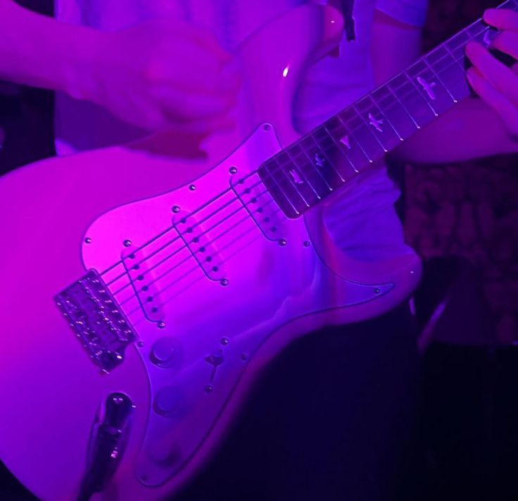 a person playing an electric guitar in a room with purple lighting on the wall behind them