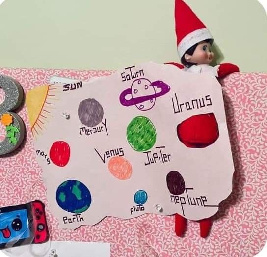 an elf is sitting on top of a table with a sign and other items around it