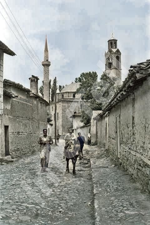 an old photo of people walking down a cobblestone street