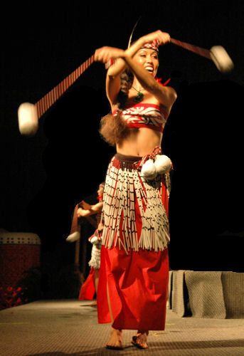 a woman in a red and white costume is dancing with two large wooden poles behind her