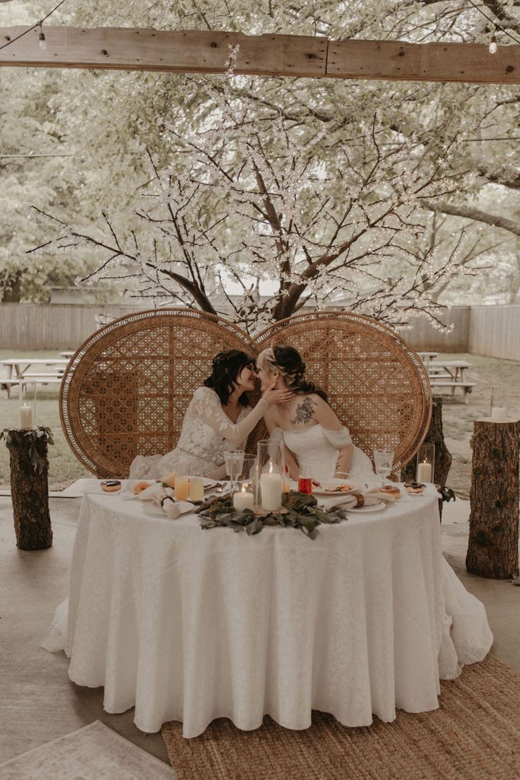 two women sitting at a table with candles in front of them and one is kissing the other