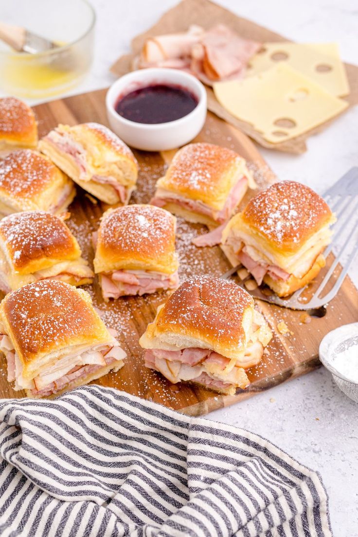 ham and cheese sliders on a wooden cutting board with dipping sauce in the background