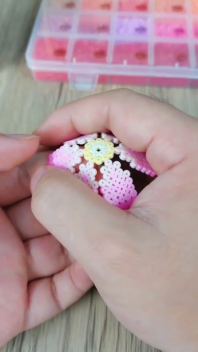 a person is holding a small pink and white flower beaded ring in their left hand