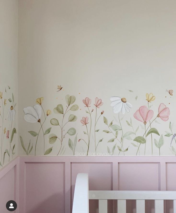 a baby's room with pink walls and flowers painted on the wall, along with a white crib