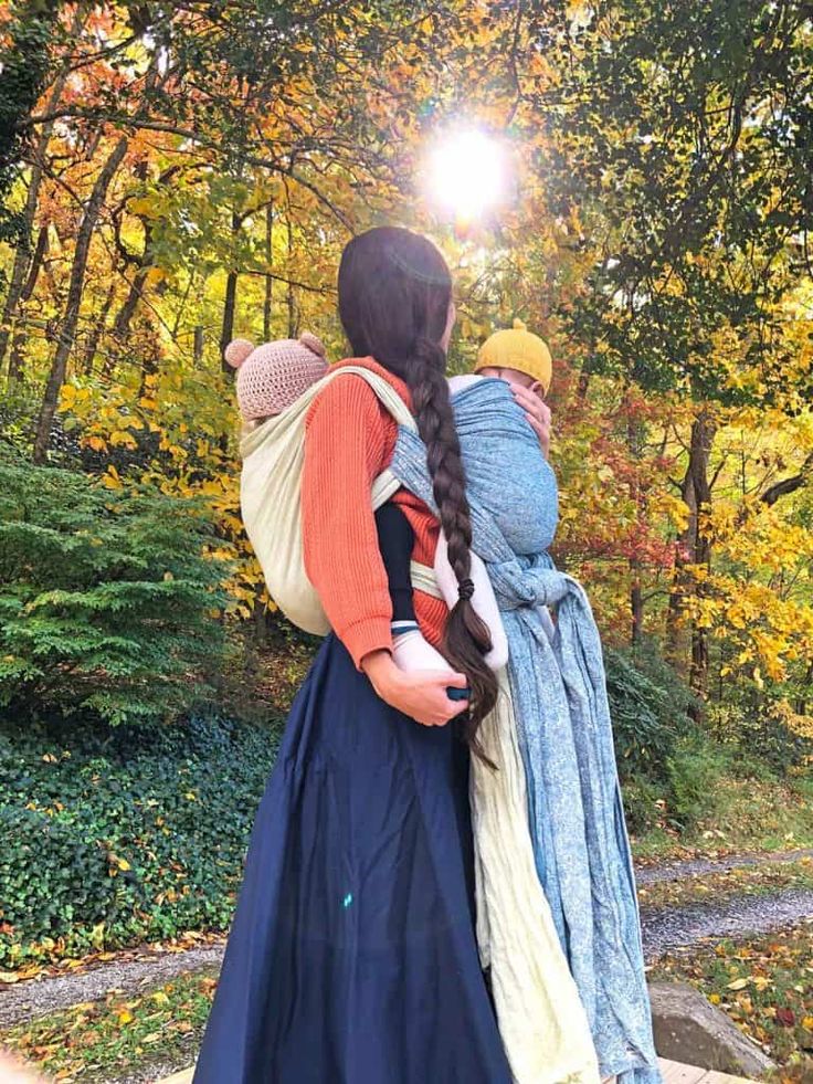 two women in long dresses are walking through the woods with their arms around each other