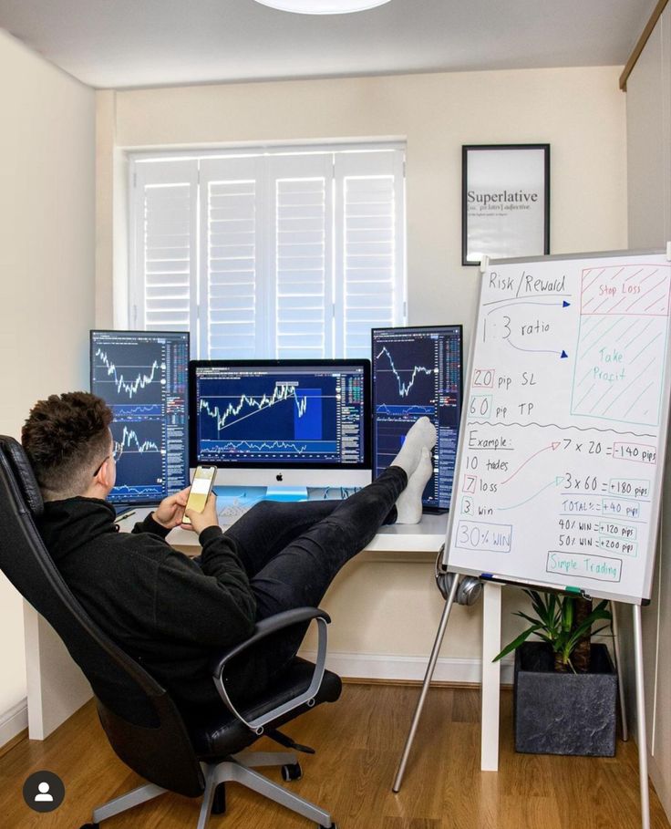 a man sitting at a desk in front of three computer monitors with graphs on them