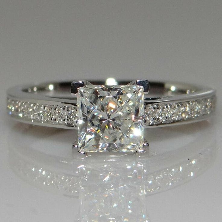 a white gold ring with a princess cut diamond and pave set diamonds on the sides