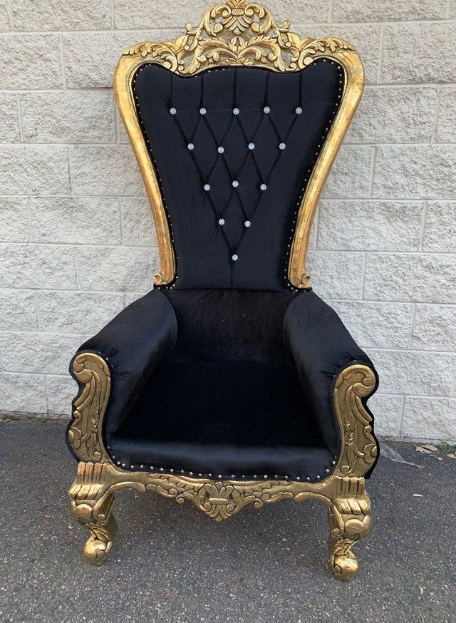 an ornate gold and black chair sitting in front of a white brick wall on the sidewalk