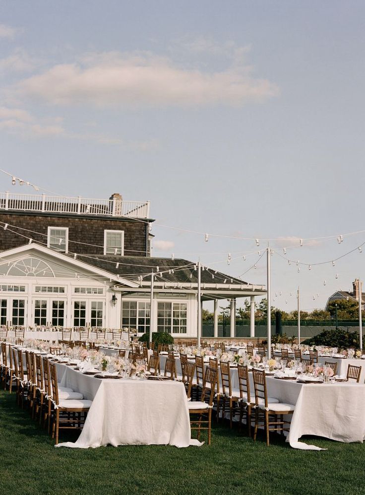 an outdoor dining area with tables and chairs set up in front of a large house