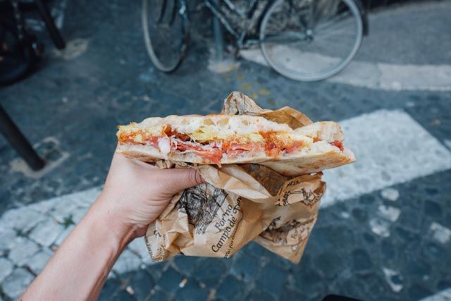 a person holding up a sandwich in front of some bikes on the street with paper wrapping around them