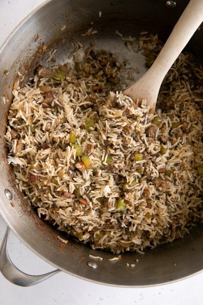 a pan filled with rice and vegetables on top of a stove next to a wooden spoon