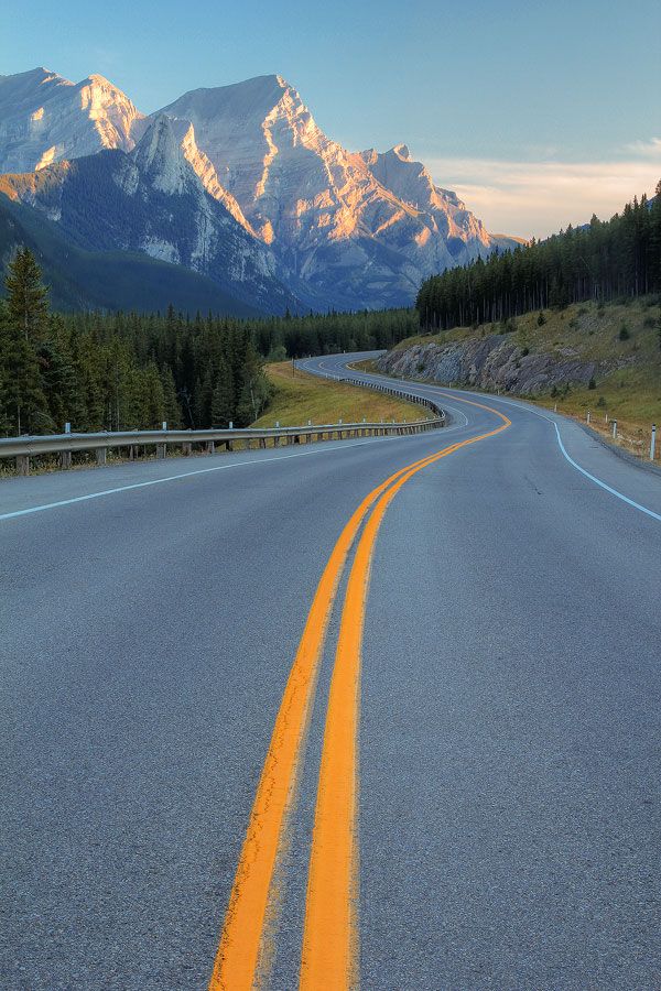 an empty road with mountains in the background and trees on both sides, at sunset