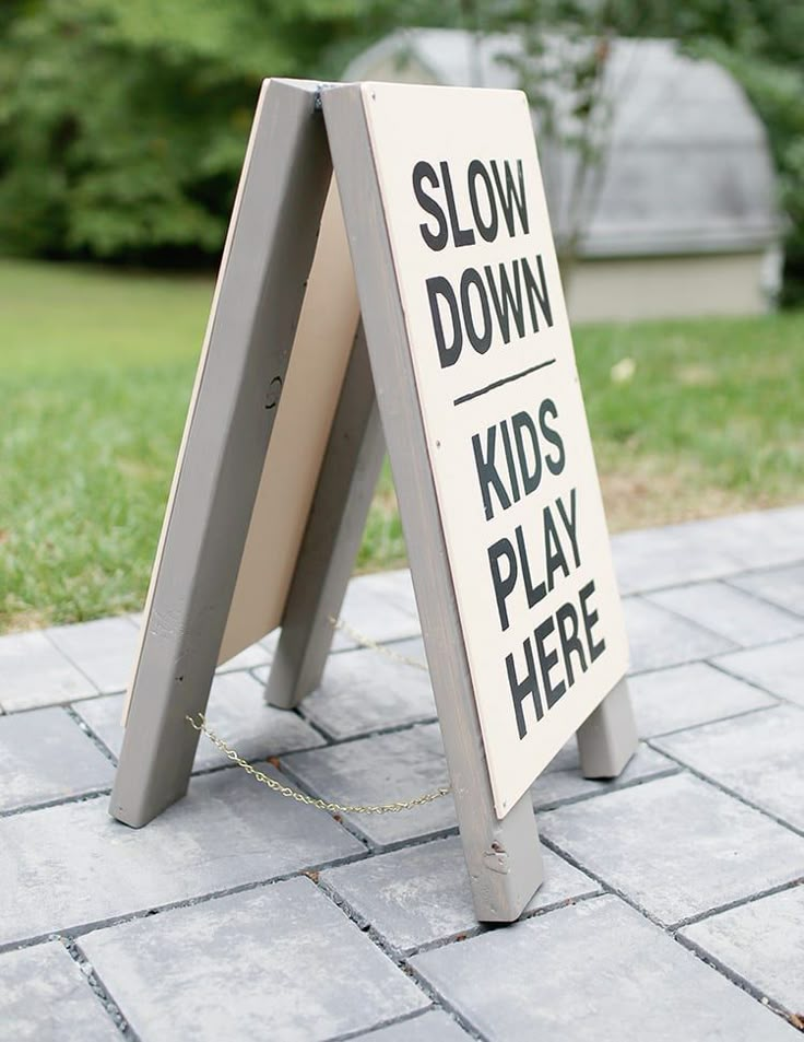 a sign that says slow down and kids play here on the sidewalk in front of some grass