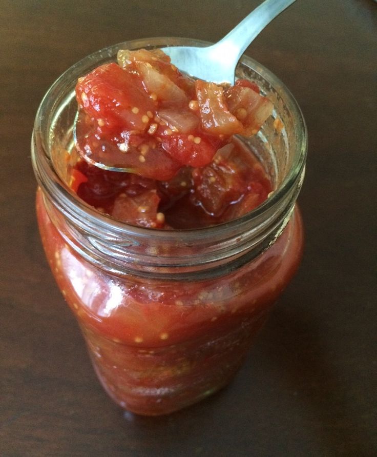 a jar filled with food sitting on top of a wooden table next to a spoon