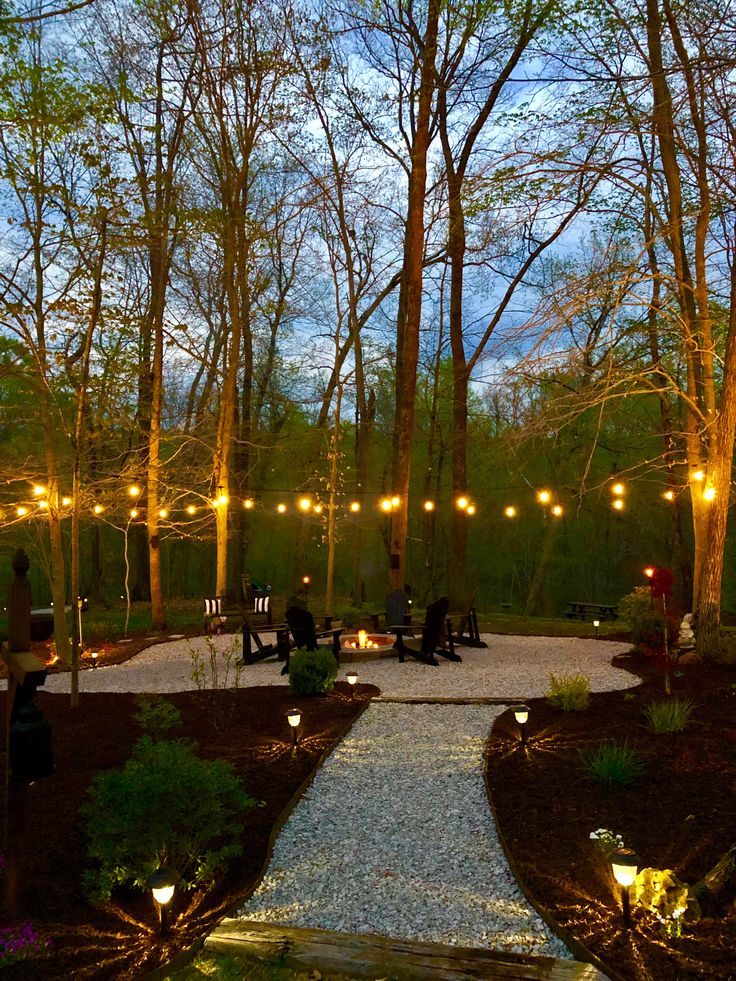 people sitting on benches in the middle of a park with lights strung from trees around them