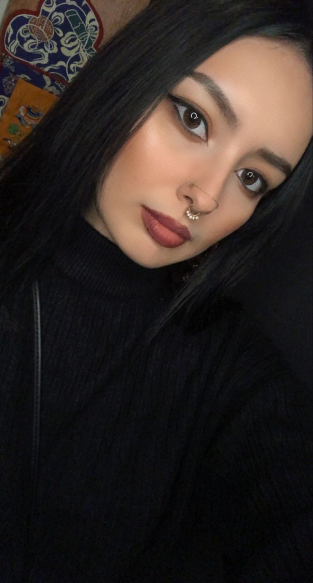 a woman with black hair and piercings on her nose posing for a selfie