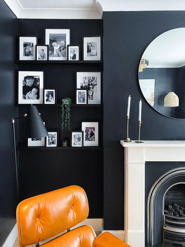 a living room with black walls and pictures on the wall, an orange chair in front of a fireplace