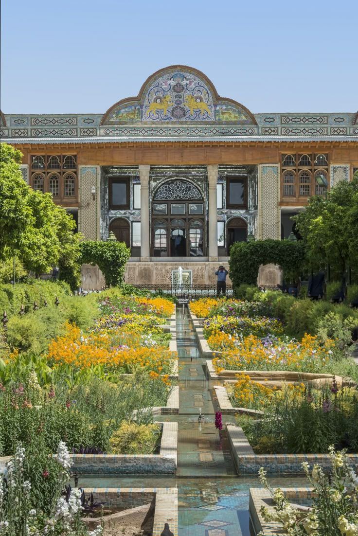 the garden is full of colorful flowers and plants in front of a large building with an ornate