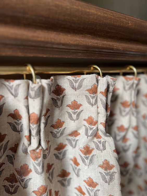 the curtain is hanging on a rod with metal hooks and has an orange flower pattern