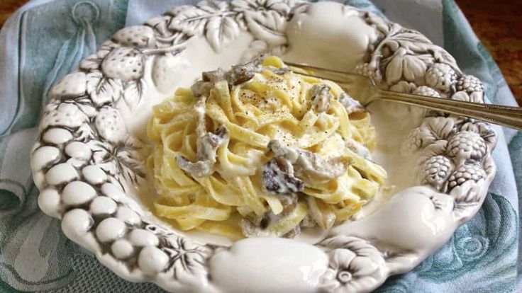 a white plate topped with pasta covered in sauce and mushrooms next to a fork on top of a blue towel