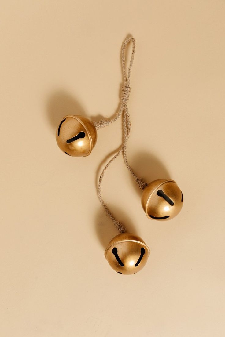 two golden bells are hanging from a string on a beige surface with no one around them