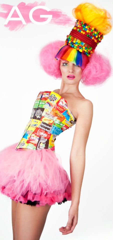 a woman with pink hair wearing a colorful dress and headpiece, posing in front of a white background