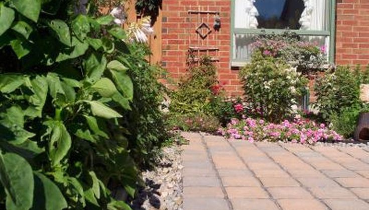 a brick walkway leading to a house with flowers in the foreground and bushes on either side